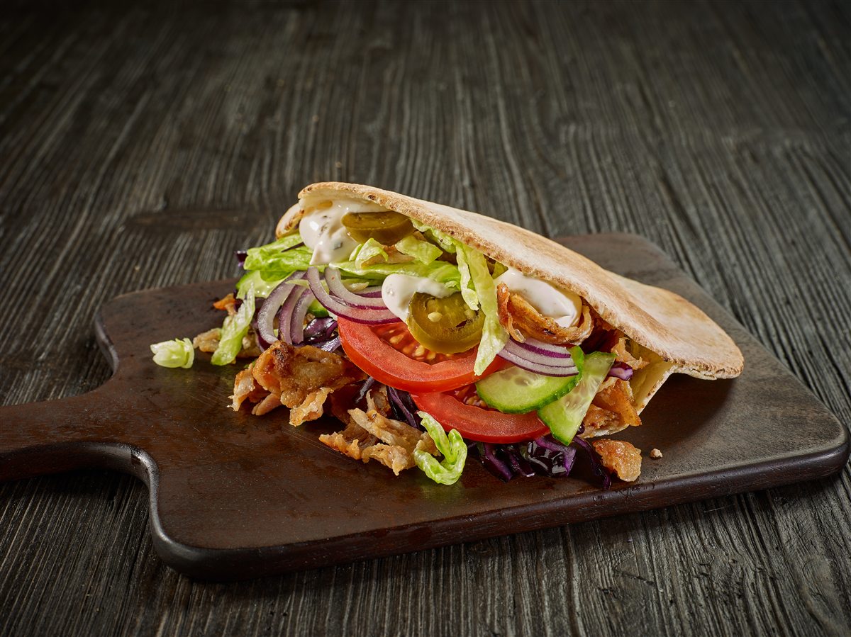 Doner kebab in warm pita with salad, chilli and garlic sauce, served on a wooden board