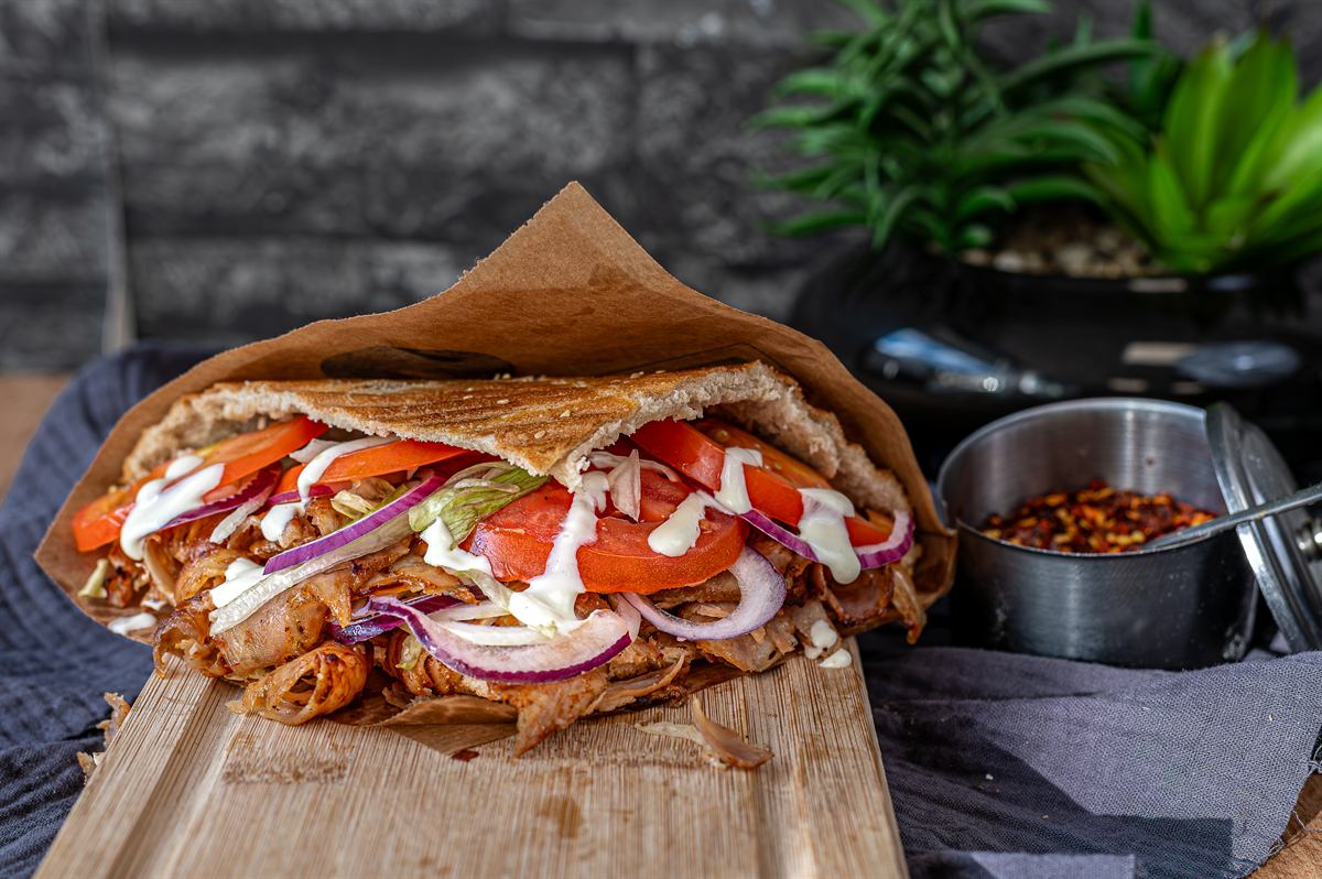Doner kebab in warm pita wrapped in paper, served on a wooden board