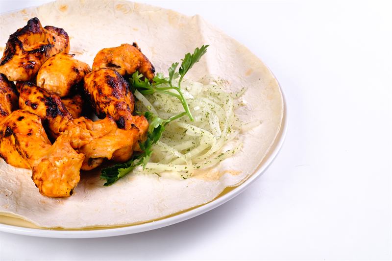 Grilled chicken pieces on flatbread with herbs and sliced onion
