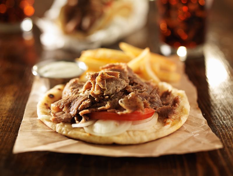 Gyro on flatbread with chips and garlic sauce on brown paper