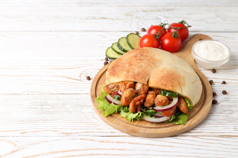 Pita bread filled with chicken and salad on a wooden serving board