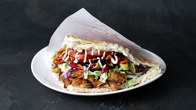 Doner kebab in flatbread served on a white plate with salad and sauces